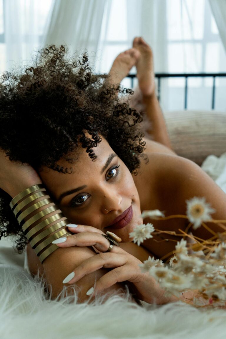 A stunning portrait of a woman with curly hair and golden bracelet lying among flowers, exuding elegance.
