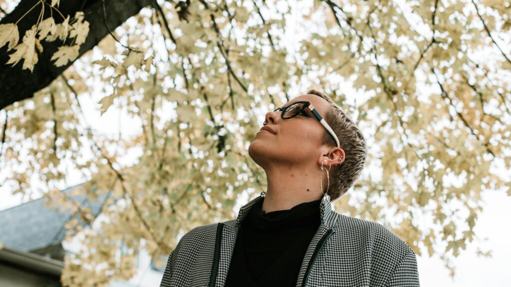 A woman wearing sunglasses enjoys the fall season under a canopy of leaves.