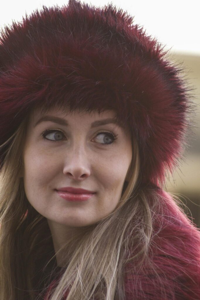 Stylish woman wearing a red fur hat, captured in a candid outdoor portrait.