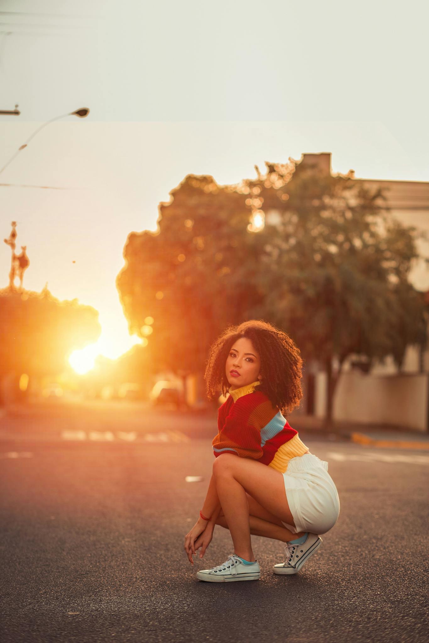 Young woman in a colorful outfit poses on a street at sunset, exuding style and confidence.