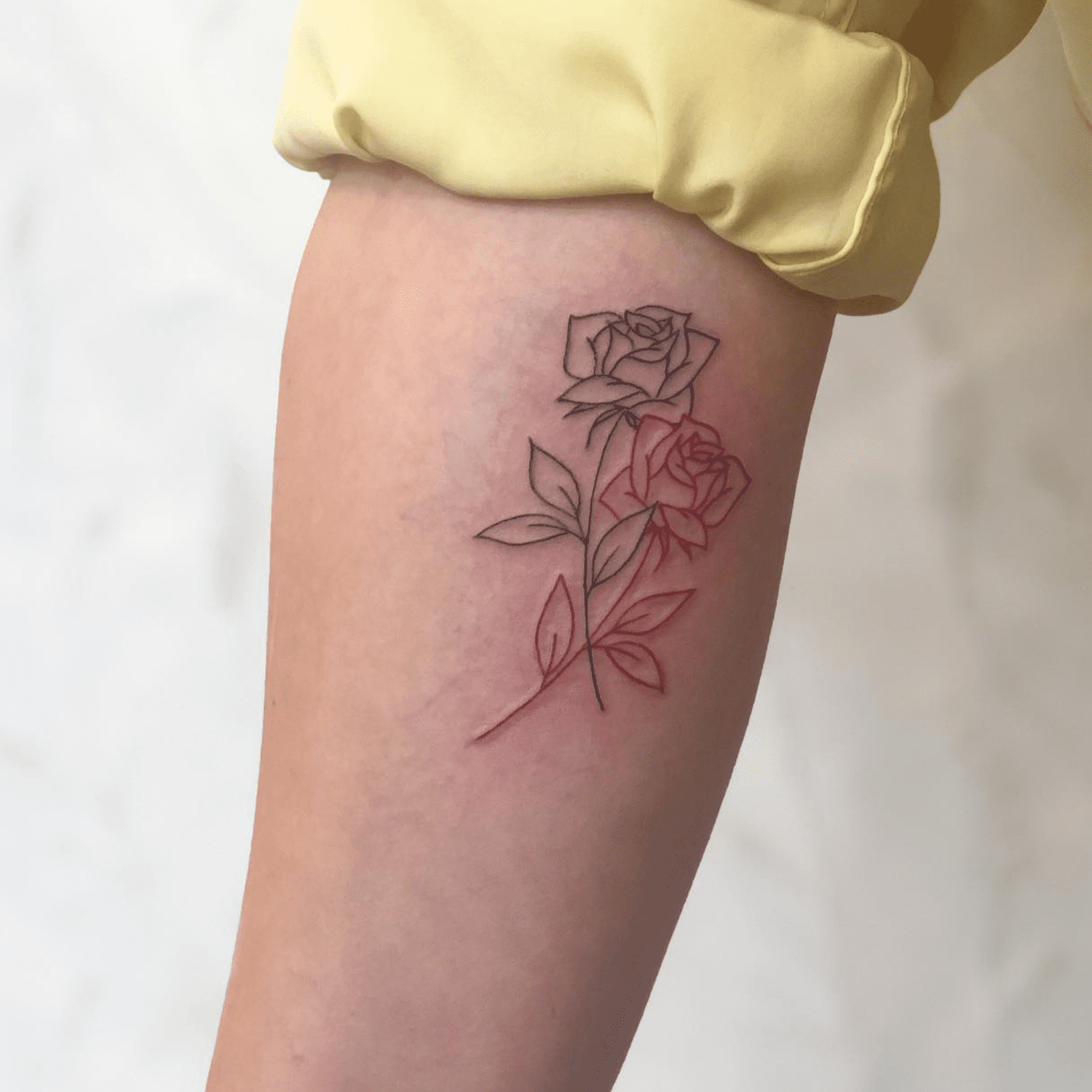 Cute arm tattoos for women: a minimalist two-tone fine line rose tattoo design featuring black and red outlines on the inner bicep.